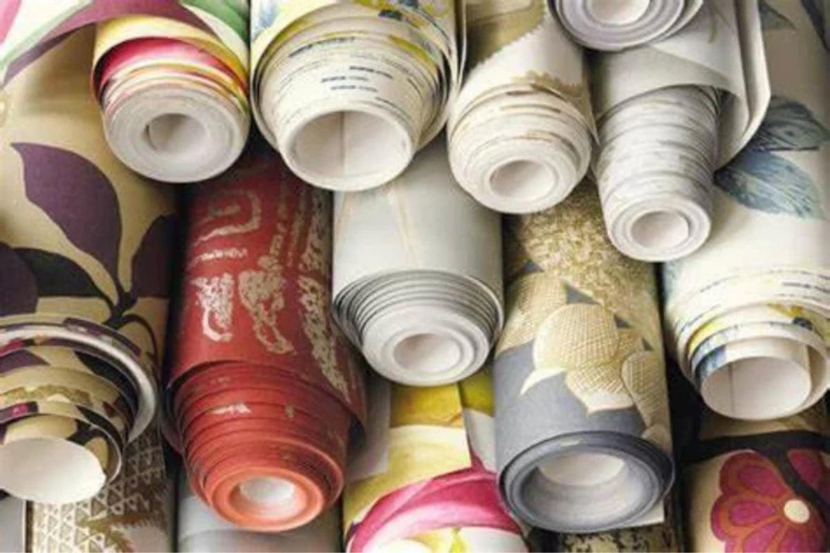 A close-up pile of rolled wallpaper or fabric samples with various floral and patterned designs in red, yellow, blue, green, and beige tones all available from Sew Chic Interiors of Brighton & Hove